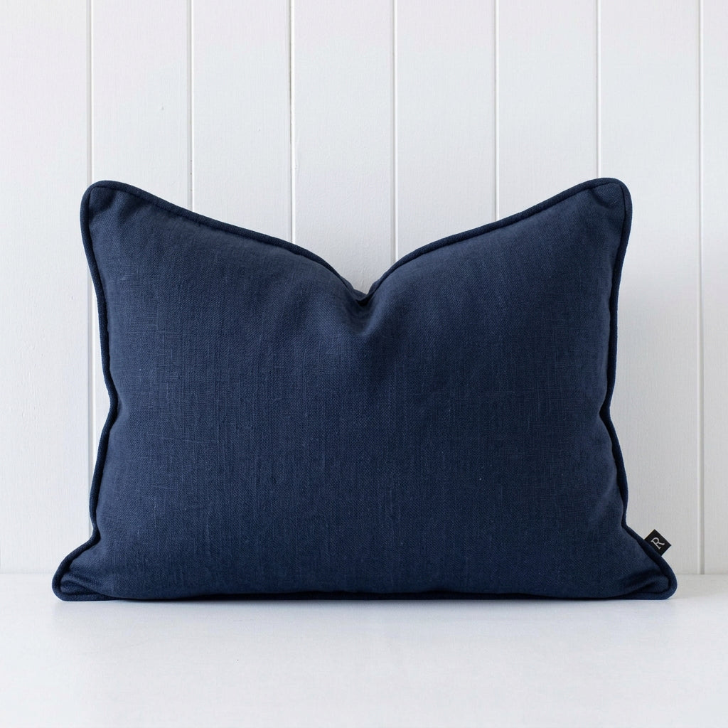 A rectangular navylumbar pillow with dark navy piping, resting against a white vertical wood paneled wall.