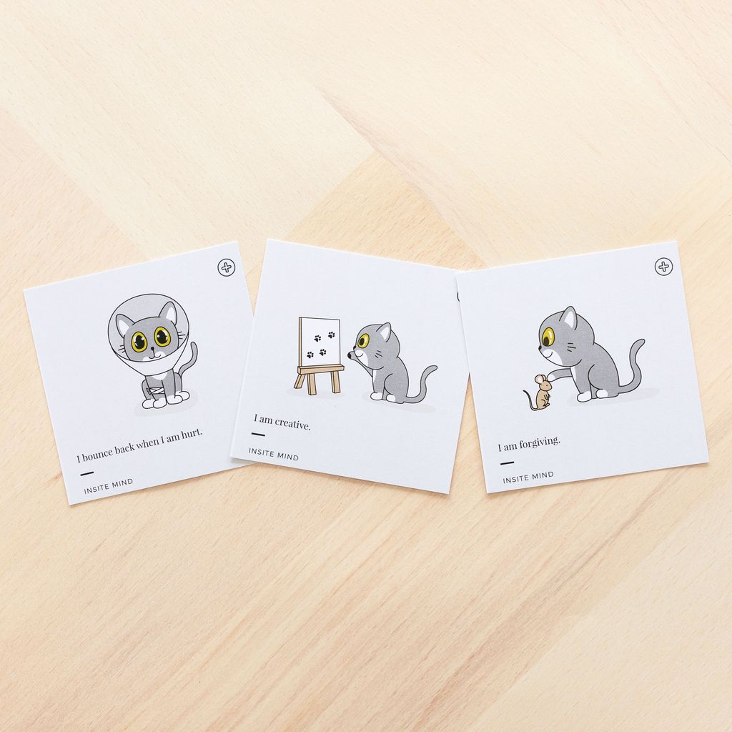 A set of three positive affirmation cards with cat illustrations, designed for kids, displayed on a wooden surface.