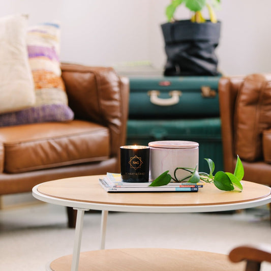 A Summer Sorbet scented candle sitting on a white round table, with a brown leather sofa and green suitcase in the background, indicating a home setting.